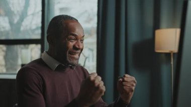 Çatı katındaki bilgisayarda oturan neşeli Afrikalı Amerikalı adamın görüntüsü. Mutlu adamın portresi sosyal medyada arkadaşlarıyla sohbet ederken heyecan verici haberler aldı. Gündüz vakti, içeride. Pozitif duygular