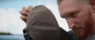 Dağ ormanlarında arabadan inen sakallı, şapkalı, ciddi bir genç adam. Mavi gökyüzü