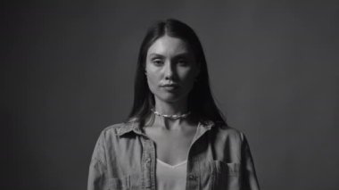 Stüdyodaki tek renkli arka planda kamera karşısında duran siyah beyaz videolu kadına bakın. Ciddi kız portresi