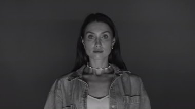 Kendine güvenen genç bir kadın stüdyoda tek renkli bir arka planda kameraya bakıyor. Ciddi bir kızın portresi. Siyah beyaz video.