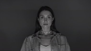 Stüdyoda çekici genç bir kadın tek renkli arka planda kameraya bakıyor. Ciddi bir kızın portresi. Siyah beyaz video