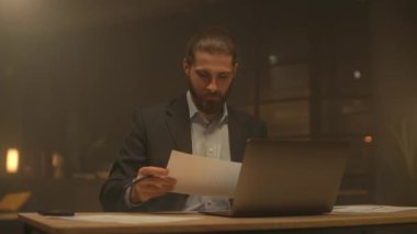 Akşam vakti sakallı genç işadamı masaya oturup kağıtlarla çalışmayı düşünür. Gece ofisindeki bilgisayarı kullan. İşine odaklan.