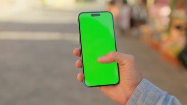 Mavi gömlekli, elinde yeşil ekranlı, arka planda bulanık sokak olan siyah akıllı telefonlu adamların görüntüsü. Krom tuş ekranında kaydıran ve dokunan adam