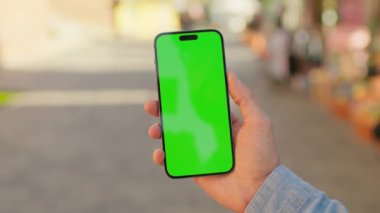 Beyaz adamın elinde akıllı telefon ile caddenin bulanık arka planında yeşil ekrana dokunduğu görüntüler. Tanınmayan adamın kot gömlekli hali. Açık havada. Modern teknoloji. Krom anahtar