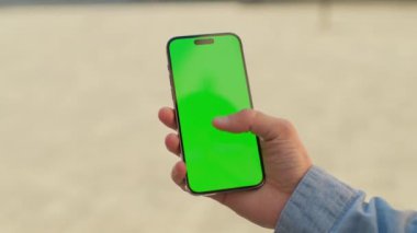 Üzerinde kot pantolon, elinde yeşil ekranlı, arka planı bulanık siyah bir akıllı telefon olan bir erkek eli resmi. Tanımlanamayan beyaz adamın ekrana dokunuşunun görüntüsü..