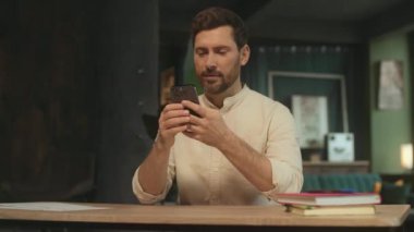 Çekici bir adam masa başında oturmuş kağıt tutarken telefonda gülümsüyor. Modern ofis. Kamera hareket ediyor. 360 Derece