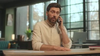 Masada oturan gülümseyen genç adam telefonda konuşuyor, mutlu ol. 360 derece. Kamera hareket ediyor