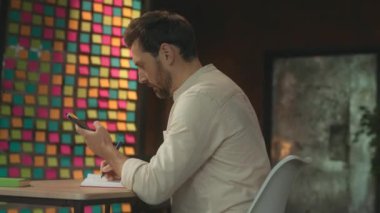 Not defterine yazan sakallı genç adam iş yerinde masa başında oturuyor. Düşünüyorum. Sosyal medyada telefon yazmayı kullan. Kamera hareket ediyor. 360 derece