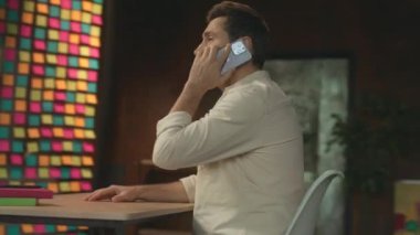 Gülümseyen işadamı masada oturmuş telefonla konuşuyor. Akıllı telefondan konuşuyor. Mutlu ol. Modern ofis. Kamera hareket ediyor. 360 derece