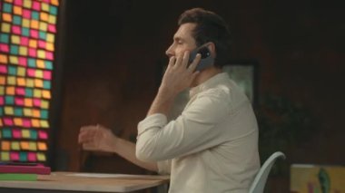 Sakallı işadamı masada oturmuş telefonla konuşuyor ve akıllı telefondan konuşuyor. Modern ofis. Sosyal medya. Kamera hareket ediyor. 360 Derece