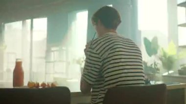 İz sürme sahnesinde hareketli enerji. Video aracılığıyla konuşurken sarı akıllı telefon kullanan gülümseyen beyaz bir genç. Mutfaktaki kahvaltı masasında oturan neşeli duygusal adam. 360 derece zaman