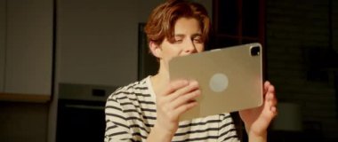 Elinde dijital tablet bulunan ve sosyal medyada gezinen kızıl saçlı neşeli beyaz kadın. Modern mutfaktaki aletlerin ekranına bakan rahat adamın portresi. Gündüz vakti. Kapalı