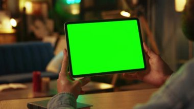 Karanlık odada elinde kaydırma tutan ve yatay yeşil ekranlı tablet bilgisayarına tıklayan bir adam. Model yap. İnternette. Teknoloji