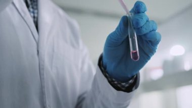 Yakın mesafeden koruyucu eldivenli bilim adamı bir tüp tutuyor ve bir ışık laboratuarının içine sıvı koyuyor. Tıp, biyoteknoloji, kimya.