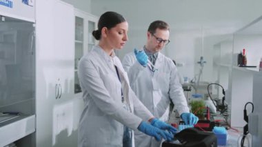 Laboratuvarda koruyucu eldivenli iki bilim adamı kadın bir ışık laboratuarında tüp tutuyor. Tıp, biyoteknoloji, kimya.