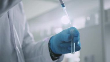 Koruyucu eldivenli bir el bilimcisi bir tüp tutuyor ve bir ışık laboratuarının içine sıvı koyuyor. Tıp, biyoteknoloji, kimya.