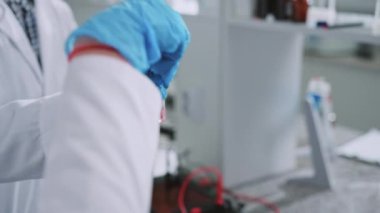 Koruyucu eldivenli iki bilim adamı bir tüp tutuyor ve ışık laboratuarında bir kutuya koyuyorlar. Tıp, biyoteknoloji, kimya.