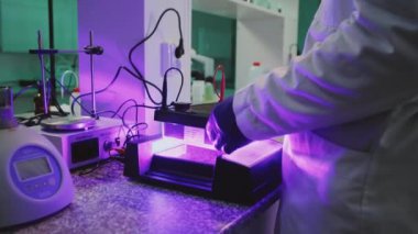 Gözlüklü bir bilim adamı ışık laboratuarında ultraviyole lambalarla çalışıyor. Tıp, biyoteknoloji, kimya.