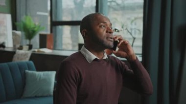 Ciddi bir iş adamının yatay olarak vurulması sohbete ve jestlere odaklandı. Rahat, modern oturma odasında akıllı telefondan konuşan Afro-Amerikalı bir adam. Kapalı