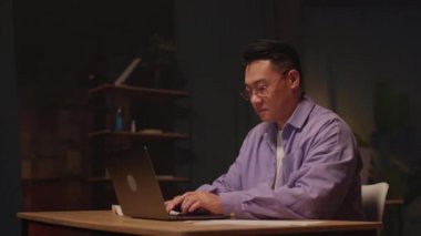 Gözlüklü genç Asyalı işadamı klavyede dizüstü bilgisayar kullanıyor. Gece mesaisi. Ekranda ciddi bir görünüm. 360 derece. Etrafta dolanıyorum.