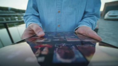Dijital tablet tutan ve ekranlara dokunan sıradan kıyafetlerle genç bir adamın görüntüsü. Yayın servisinden film seçen bir adam. Video uygulaması. Açık havada.