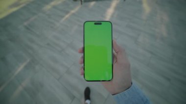 Açık hava görüntüsü, yeşil ekran yürüyüşlü, el ele tutuşan ve dikey telefonu kaydıran adam görüntüsü. Gün ışığında gölün arkasında. Akıllı telefondan yazıyorum.