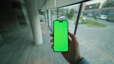 Kapalı alan görüntüsü, yeşil ekranlı, el kamerasının tutuşu ve dikey olarak telefonu kaydırması. Arka planda büyük pencereli modern alan. Akıllı telefondan yazıyorum.