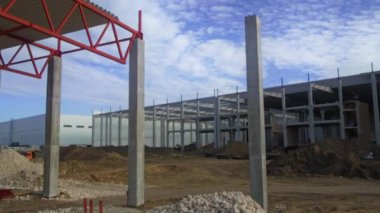 Hareketli ve dinamik bir inşaat alanı beton sütunlar ve çelik iskelet sergiliyor, hepsi bulutlu bir gökyüzünün altında.