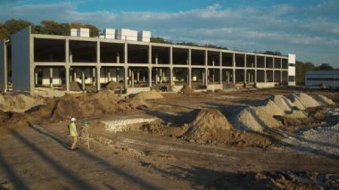 Gelişmekte olan bir inşaat alanı, çeşitli toprak ve makinelerin ortasındaki modern bir binanın iskeletini gösteriyor.