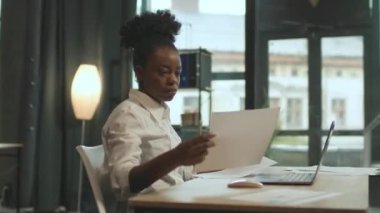 Sandalyede oturan çekici Afro-Amerikan kadın ofiste bilgisayarla çalışıyor. Çok ciddiyim. Kamera hareket ediyor. 360 derece