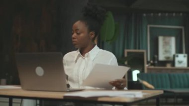 Sandalyede oturan ciddi bir Afro-Amerikalı kadın ofiste bilgisayarla çalışıyor. Kamera hareket ediyor. 360 derece