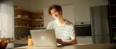 Enerjik hareketler, masada oturup dizüstü bilgisayar ekranına bakan neşeli, beyaz bir gencin görüntülerini takip ediyor. Adam mutfakta sohbet ederken gülüyor ve portakal suyu içiyor.