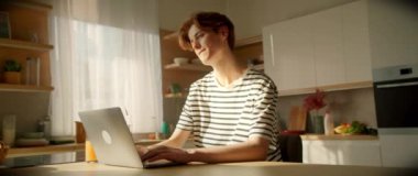 Mutfakta dizüstü bilgisayarla masada oturan düşünceli beyaz bir adam. Klavyede yazı yazan ve ekrana bakan yakışıklı bir adamın görüntüsü. - Eve. Gündüz vakti. İletişim konsepti. İz sürme