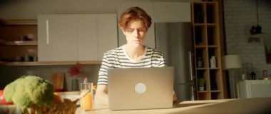 Yorgun genç adam mutfakta dizüstü bilgisayar kapatıyor. Yakışıklı erkek öğrenci işini bitiriyor. Önde sebzeli bir masa. Parallaks etkisi. Optik yanılsama. Kamera hareket ediyor. Kapalı