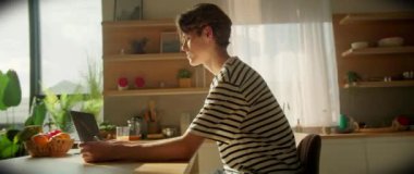 Klavyeye yazı yazan düşünceli, Kafkas odaklı bir adam. Genç erkek yazar mutfakta oturuyor ve dizüstü bilgisayarla çalışıyor. Modern rahat iç mekan. 360 derecelik izleme atışı. Kapalı