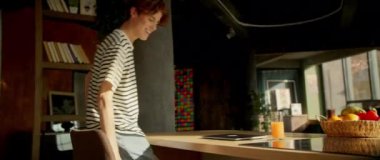 Çizgili tişörtlü çekici beyaz adam evde dizüstü bilgisayarla masada oturuyor. Adam modern mutfakta vakit geçiriyor. Çevrimiçi iletişim. Çekim sırasında iz sürüyorum. Kapalı