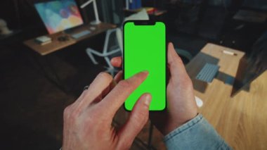 Karanlık bir odada dikey yeşil ekranlı adam tutucuları ve kaydırmalı telefonları kapatın. Cihaz. Akıllı telefonmuş. Model aygıtı