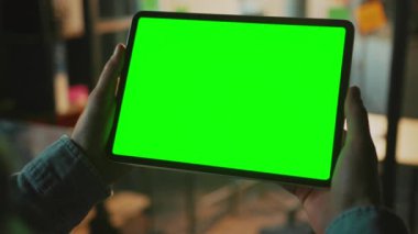 Elinde yeşil ekranlı siyah dijital tablet tutan adam. Kotlu tişörtlü tanınmayan bir adam evdeki platformda video izleyen bir alet kullanıyor. Dairenin arka planı bulanık. İyi akşamlar.