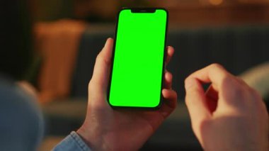 Bulanık arka planda yeşil ekranlı akıllı telefon tutan adam. Modelleme. Boş ekran ile kapalı alanda telefon çekimleri. Krom anahtar. Modern teknoloji konsepti. Cep telefonu, aygıt