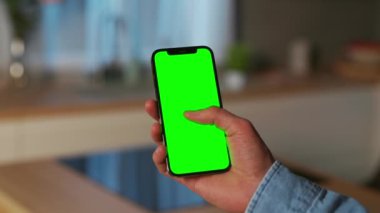 Sağ elinde yeşil ekranlı siyah akıllı telefon tutan, tanımlanamayan beyaz bir adamın görüntüsü. Alet ekranına bakan, sosyal medyada gezinen bir adam. İnternet bağımlılığı kavramı