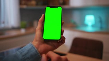 Kotlu ceketli bir erkeğin elinde yeşil ekranlı akıllı bir telefonla mutfakta otururken ki görüntüsü. Bulanık arka planda cep telefonu kullanan bir adam. Dokun, göster. Krom anahtar kavramı. Kapalı