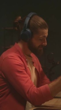 Mikrofonun önünde oturmuş dinleyicilerle konuşan enerjik genç bir adamın görüntüsü. Adam akşam saatlerinde modern ofiste podcast yaparken dizüstü bilgisayar ekranına bakıyor.