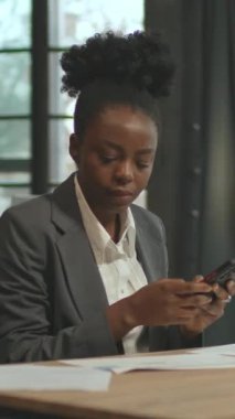 360 derecelik hızlandırma. Gri takım elbiseli Afro-Amerikalı iş kadını laptopuyla masada oturuyor ve akıllı telefon kullanıyor. Çalışan genç bir kadın. İz sürme sahnesinde hareketli enerji. Başarılı kız.