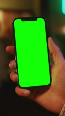 Eller kapalı alanda dikey yeşil ekranlı cep telefonu tutuyor ve kullanıyor. Sosyal medya. Model