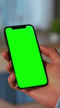 Erkek eli ceketi giyerken çekilmiş bir fotoğraf. Elinde yeşil ekranlı akıllı bir telefon var. Mutfağın bulanık arka planında izole edilmiş. İnternette yemek fikirlerini okuyan tanınmayan bir adam.