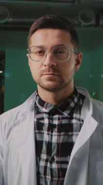 Gözlüklü, koruyucu eldivenli, beyaz üniformalı yakışıklı, neşeli bilim adamı laboratuarın içindeki kameraya bak. Araştırmacı işçi.