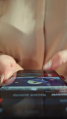 Avrupa - 17 Mart 2022: Bej bluzlu, tanınmayan genç bir kadının akıllı telefondan online alışveriş yapıp cihaz ekranına baktığı görüntüler. Kız alışveriş uygulamasında geziniyor, ürünleri tarıyor