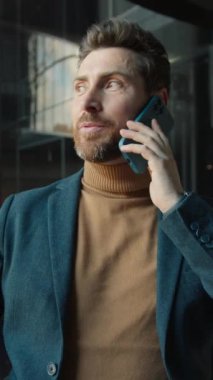 Yakından şık ceketli çekici bir genç adam telefonda konuşuyor. Etrafa bakınıyor ve iş merkezinde mutlu oluyor. Arka planda modern iç tasarım