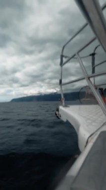 Huzurlu ve sakin bir okyanus sahnesi, bulutlu bir gökyüzünün altında suyu pürüzsüz bir şekilde kesen bir teknenin eğildiği.