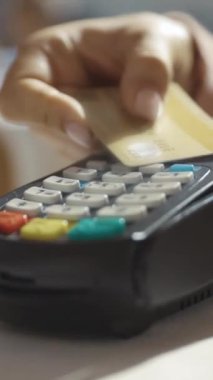 Elektronik ödeme işlemi sırasında bir el kart okuyucusunun üzerinde ödeme kartı tutuyor.